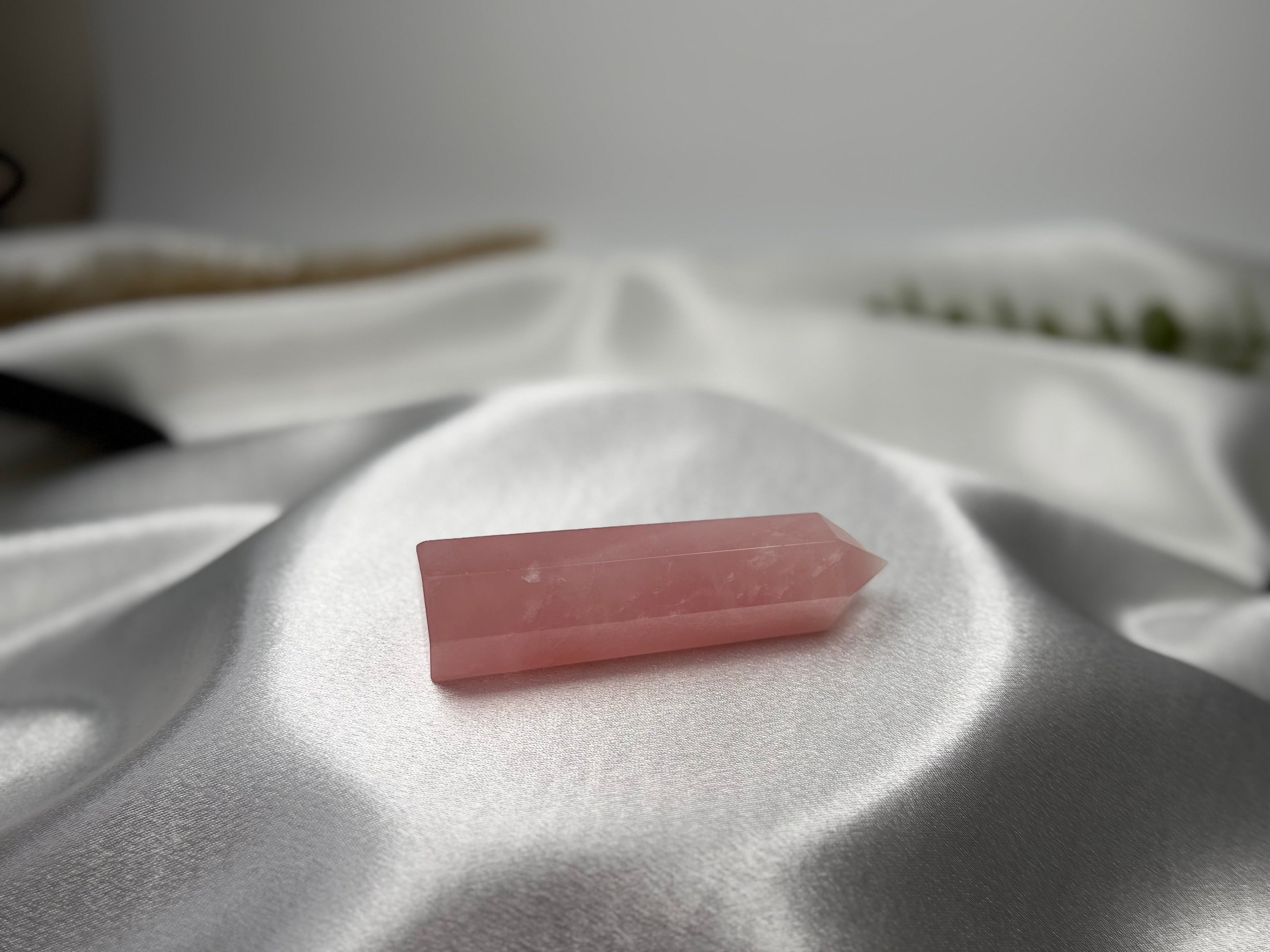 Treasured Energies polished rose quartz crystal tower point resting on soft white satin fabric