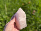 Treasured Energies large rose quartz crystal tower with a polished point and raw base held against a green background