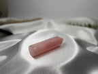 Treasured Energies polished rose quartz crystal tower on a soft white satin fabric background