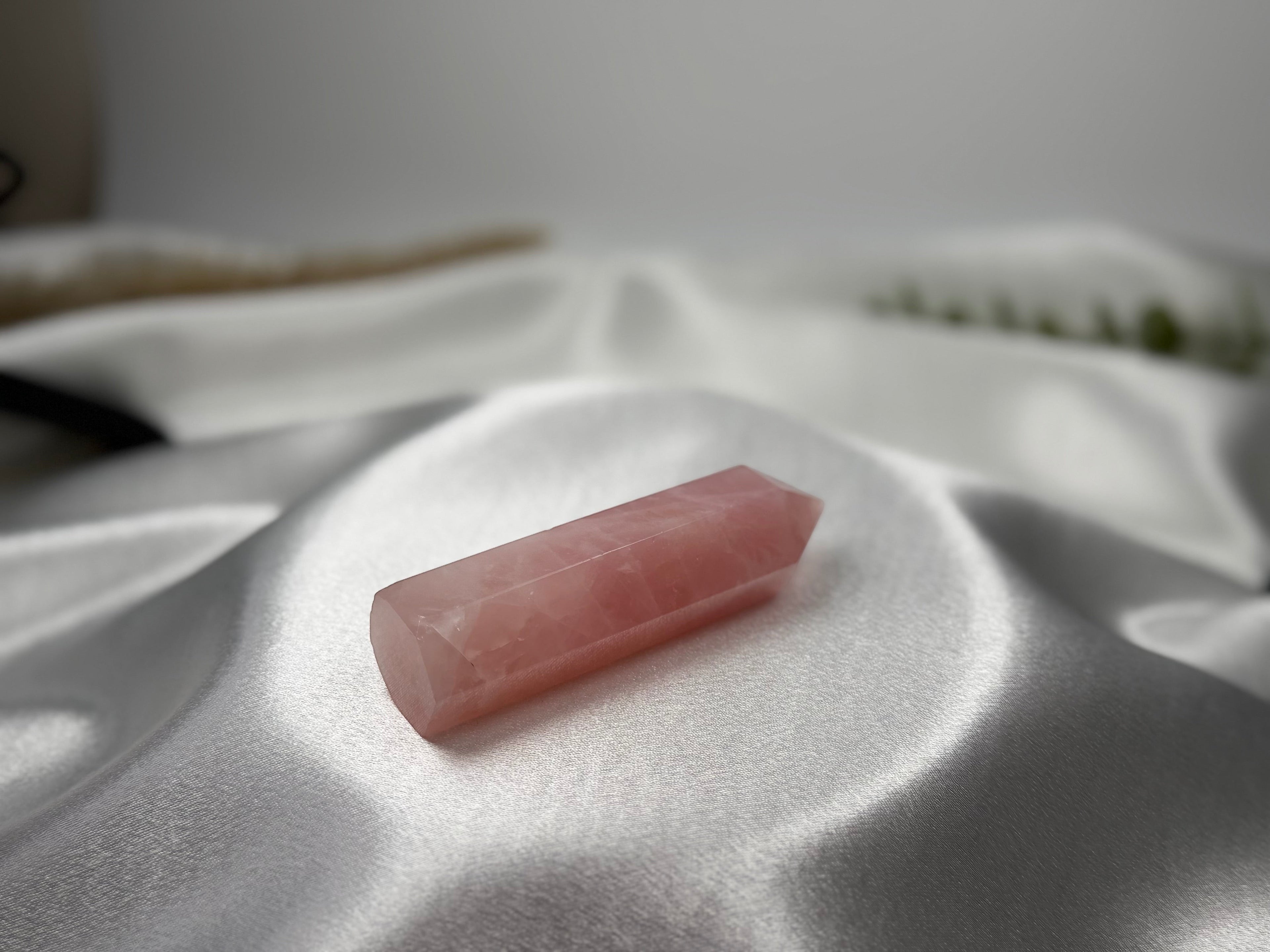 Treasured Energies polished rose quartz crystal tower on a soft white satin fabric background