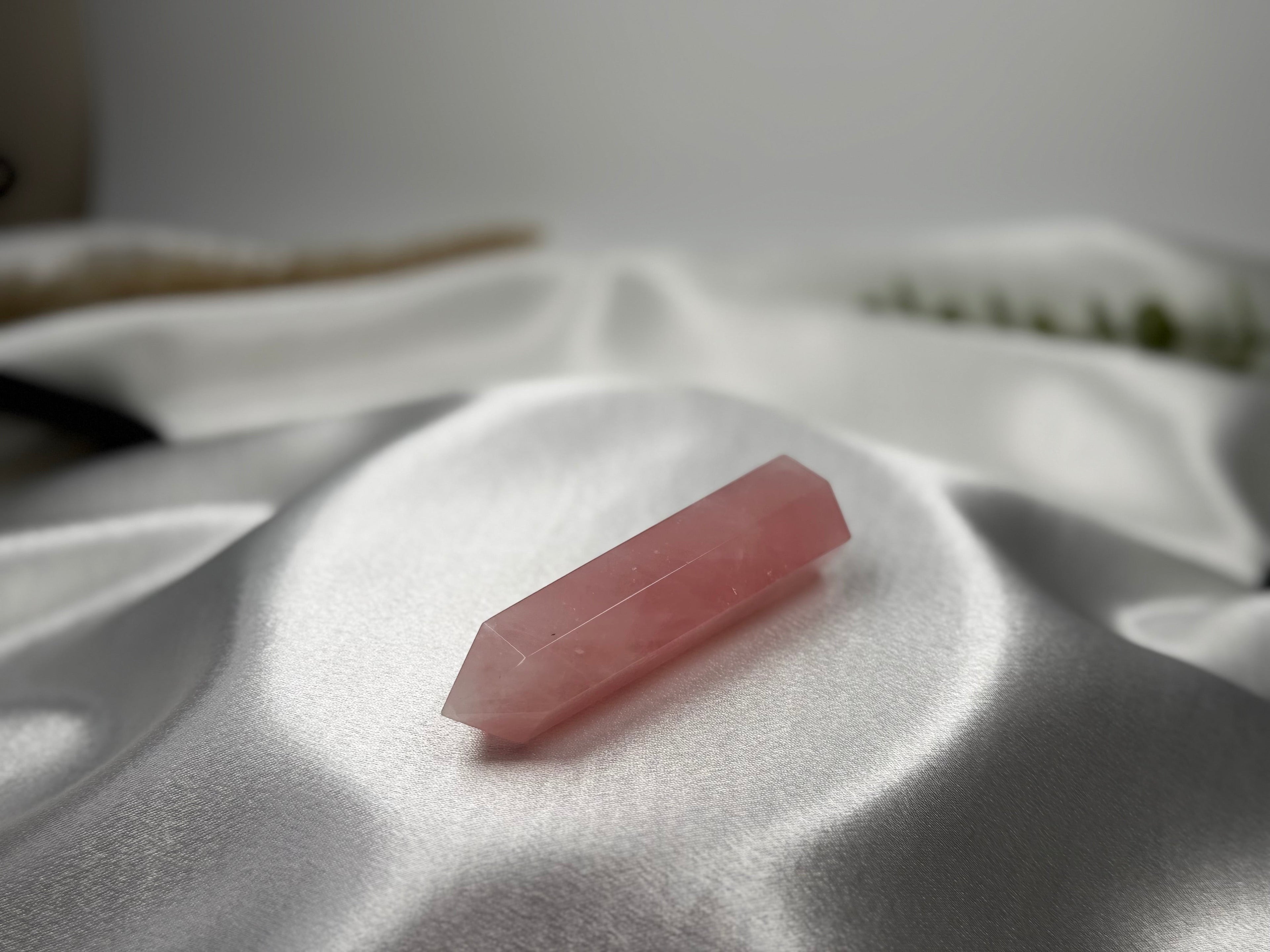 Treasured Energies rose quartz crystal tower with a pointed tip resting on soft white satin fabric.