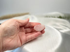 Treasured Energies smooth polished rose quartz tumbled stone held in a palm against a soft white satin background