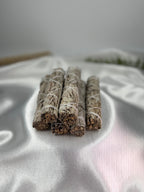 Treasured Energies white sage smudge sticks bundled with white string for smudging on a soft white satin fabric background