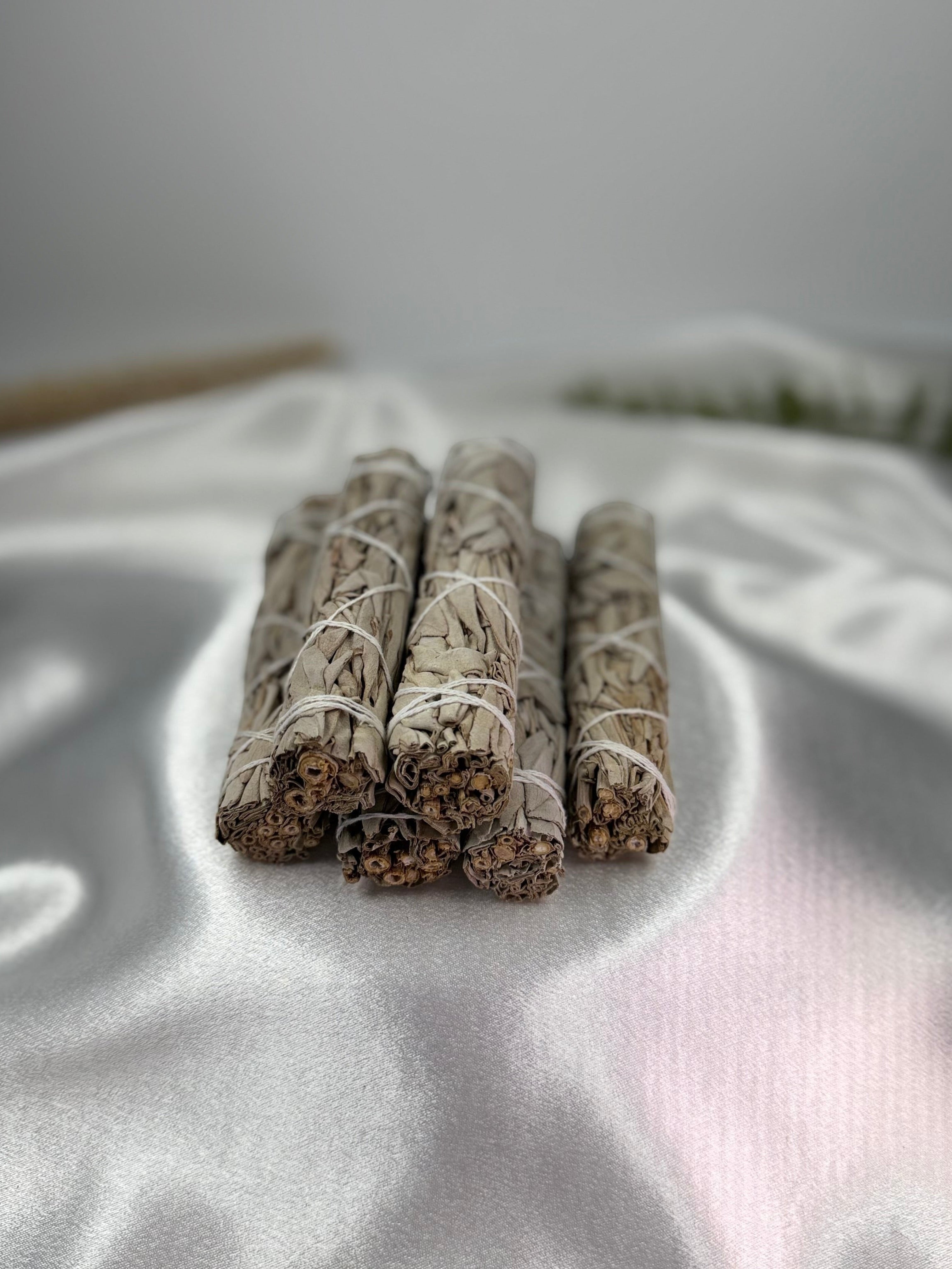 Treasured Energies sage sticks bundled with white string for smudging on a soft white satin fabric background