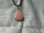 Treasured Energies scolecite crystal pendant in a sterling silver setting on a black cord against a textured fabric.