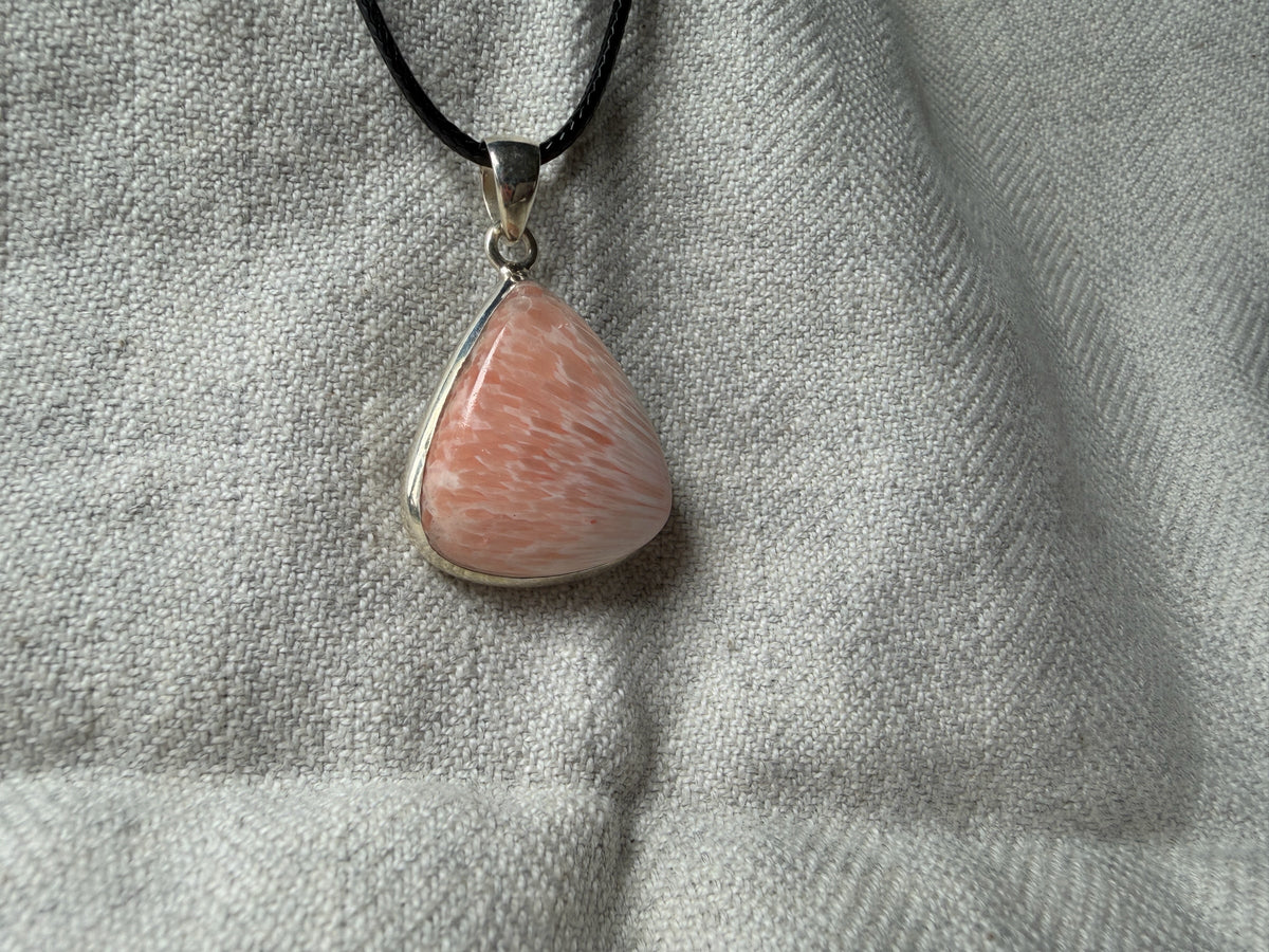 Treasured Energies scolecite crystal pendant in a sterling silver setting on a black cord against a textured fabric.