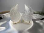 Treasured Energies pair of carved white selenite angel wings on gold stands displayed on a satin fabric surface.