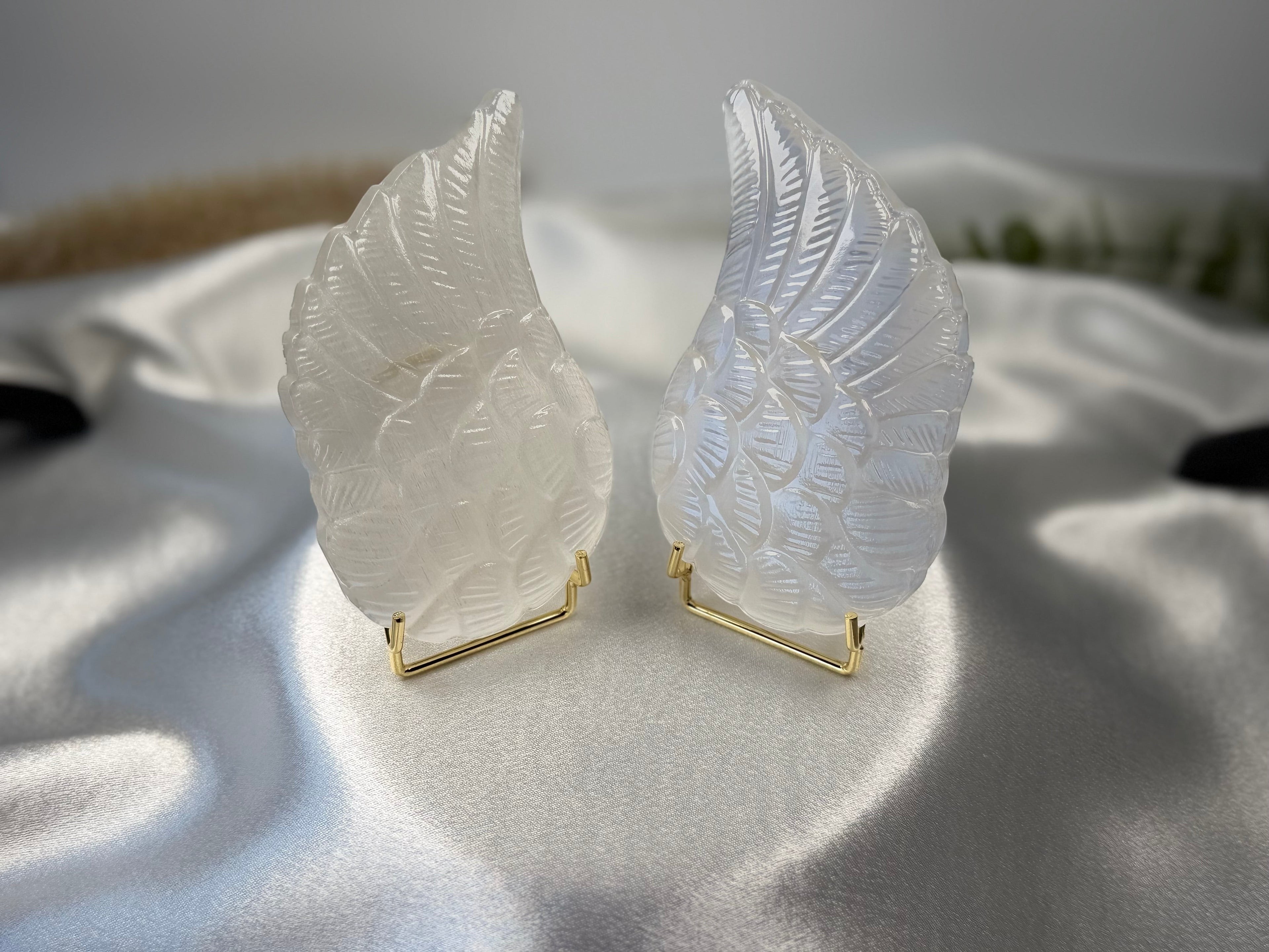Treasured Energies pair of carved white selenite angel wings on gold stands against a soft satin background