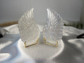 Treasured Energies pair of carved white selenite angel wings on small gold stands against a white satin background.
