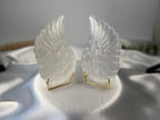 Treasured Energies pair of carved white selenite angel wings on small gold stands against a white satin background.