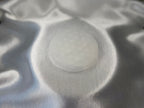 Treasured Energies 8cm round white selenite charging plate with a delicate engraved flower of life pattern on satin