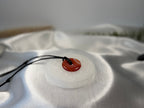 Treasured Energies 8cm round white selenite charging plate with engraved flower of life pattern holding a red stone pendant