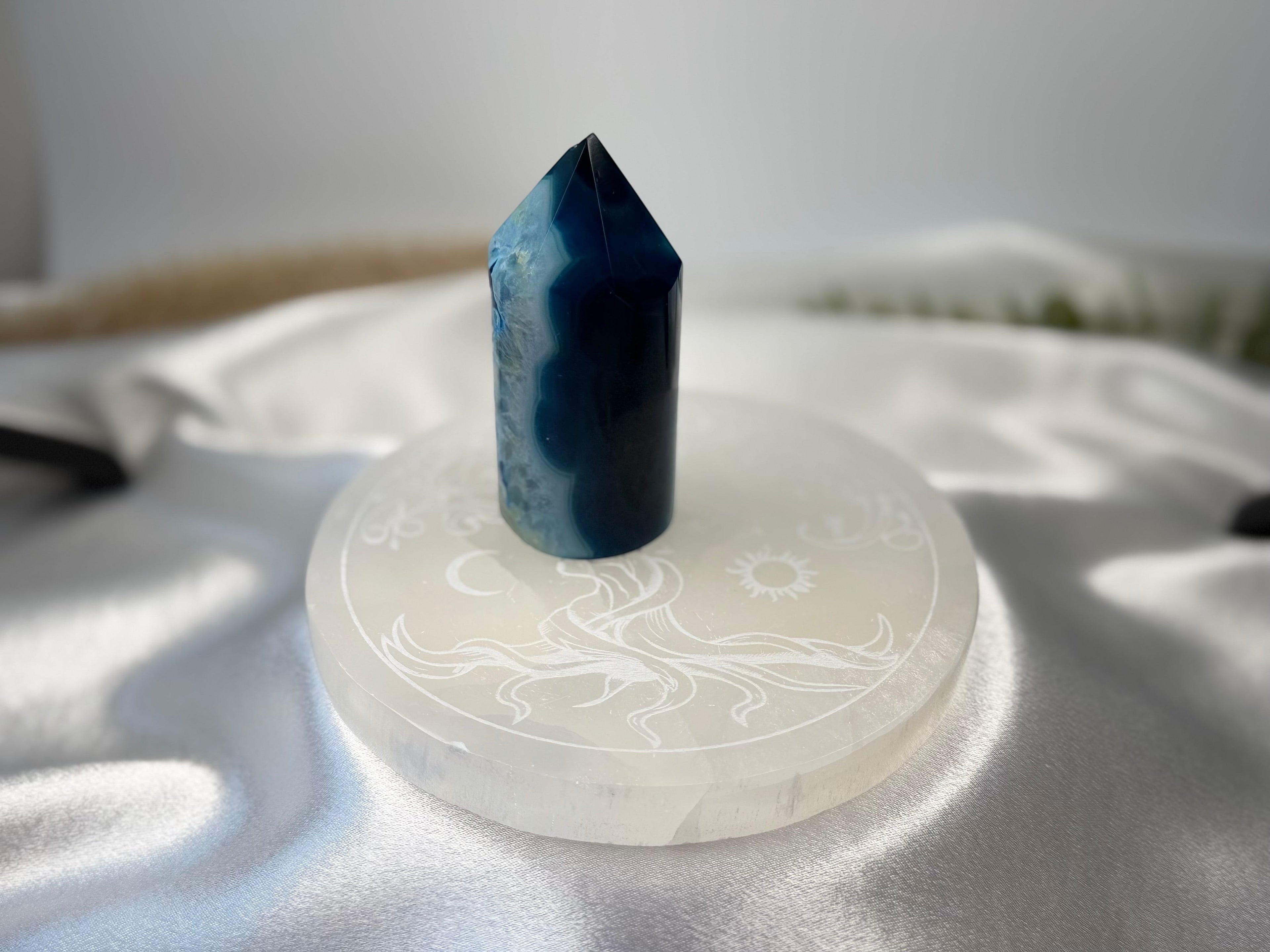 Treasured Energies 14cm round white selenite charging plate with celestial engraving holding a blue agate crystal tower