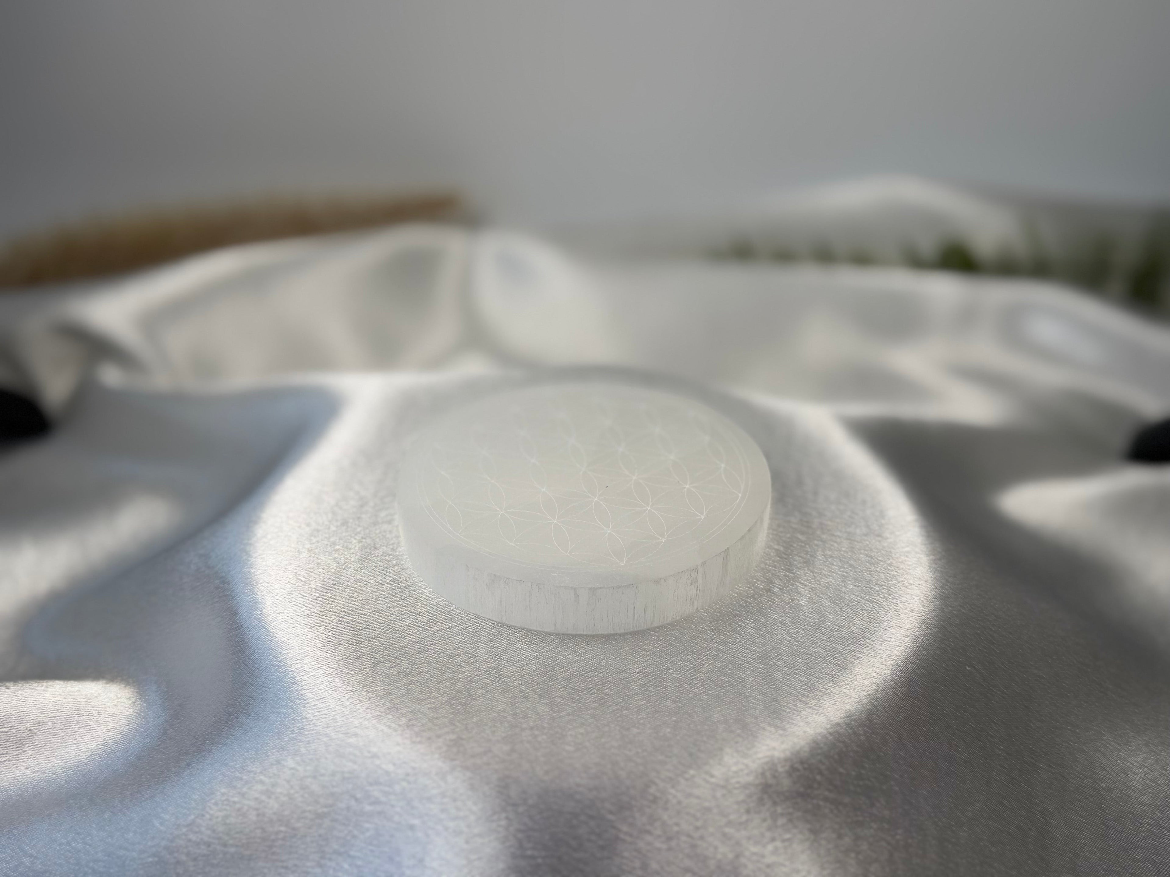 Treasured Energies 8cm round white selenite charging plate with sacred geometry engraving on a silky white fabric.