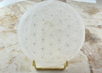 Treasured Energies 8cm round white selenite charging plate with an engraved flower of life pattern on a gold stand.
