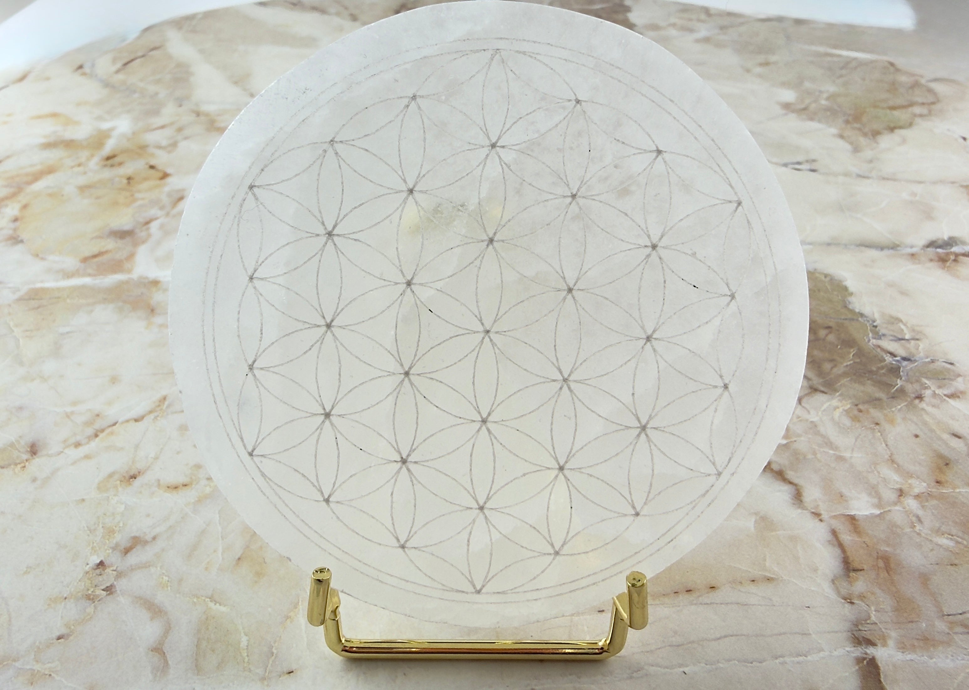 Treasured Energies 8cm round white selenite charging plate with an engraved flower of life pattern on a gold stand.