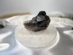 Treasured Energies round white selenite charging plate with engraved design holding a dark smoky quartz crystal cluster