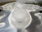 Treasured Energies hand carved white selenite crystal bowl resting on a soft, shimmering silver satin fabric.