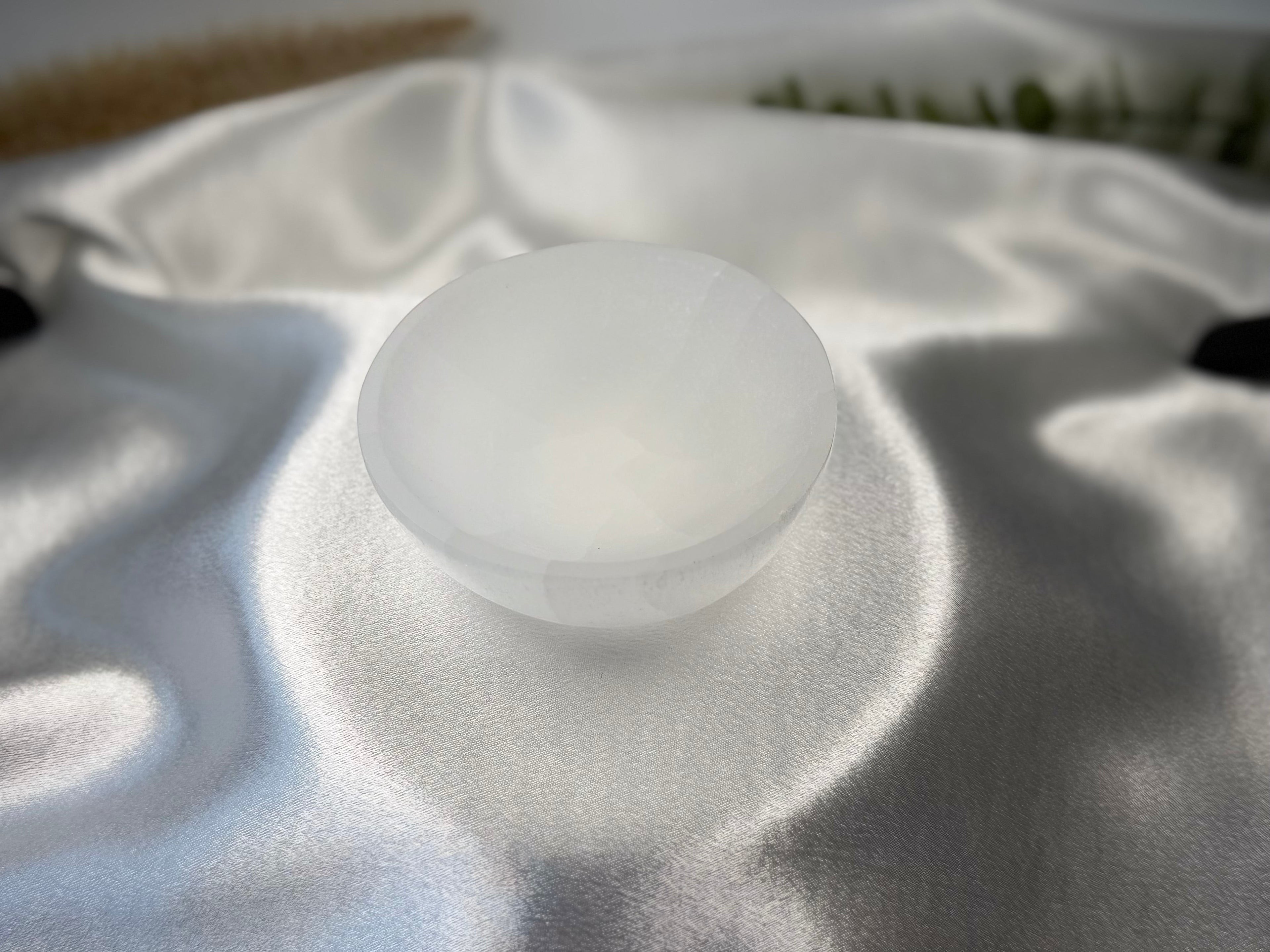 Treasured Energies hand carved white selenite crystal bowl resting on a soft, shimmering silver satin fabric.