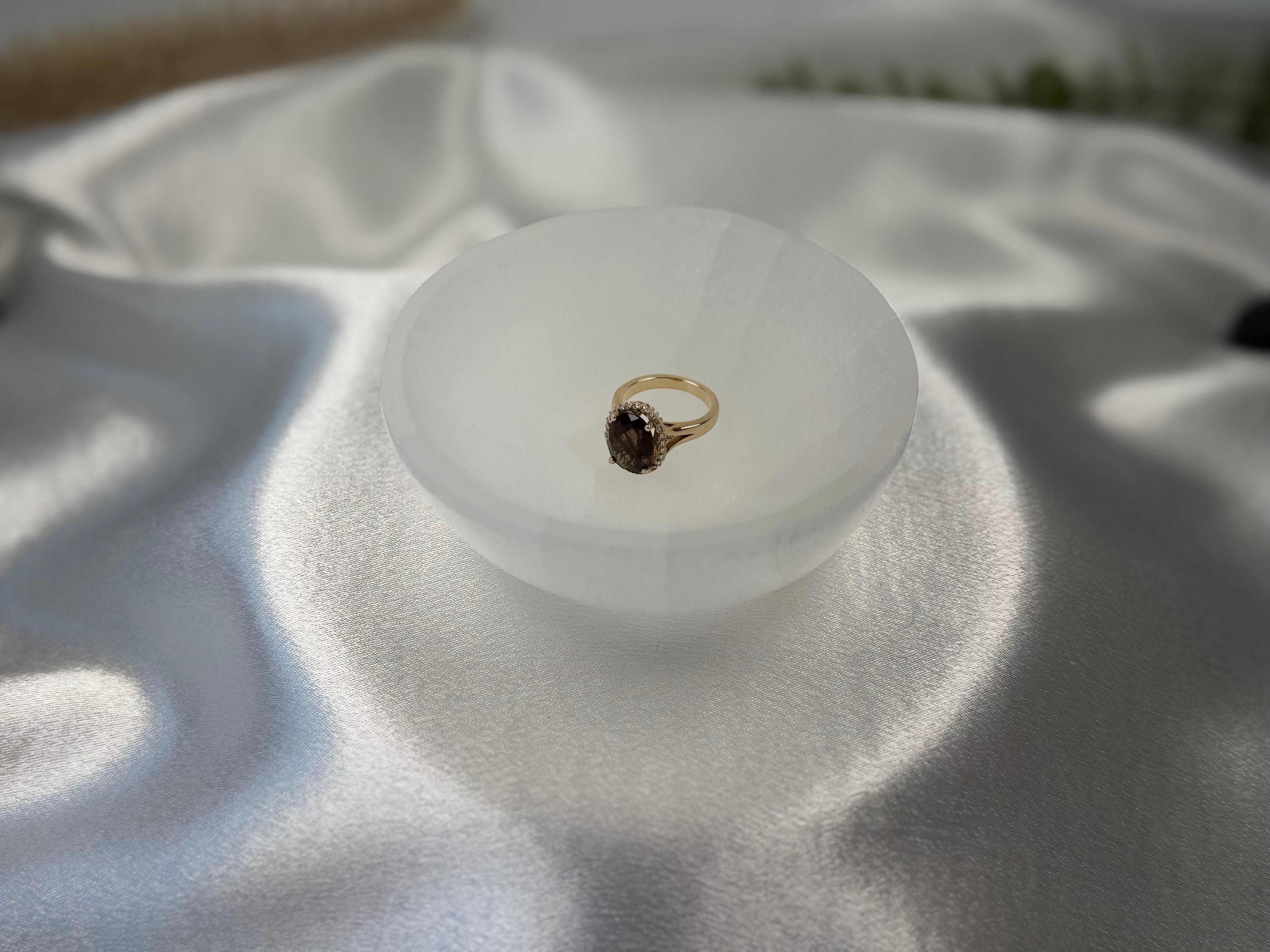 Treasured Energies hand carved white selenite crystal bowl holding a gold ring on a white satin fabric background