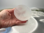 Treasured Energies hand carved white selenite crystal bowl held in a hand against a soft satin background