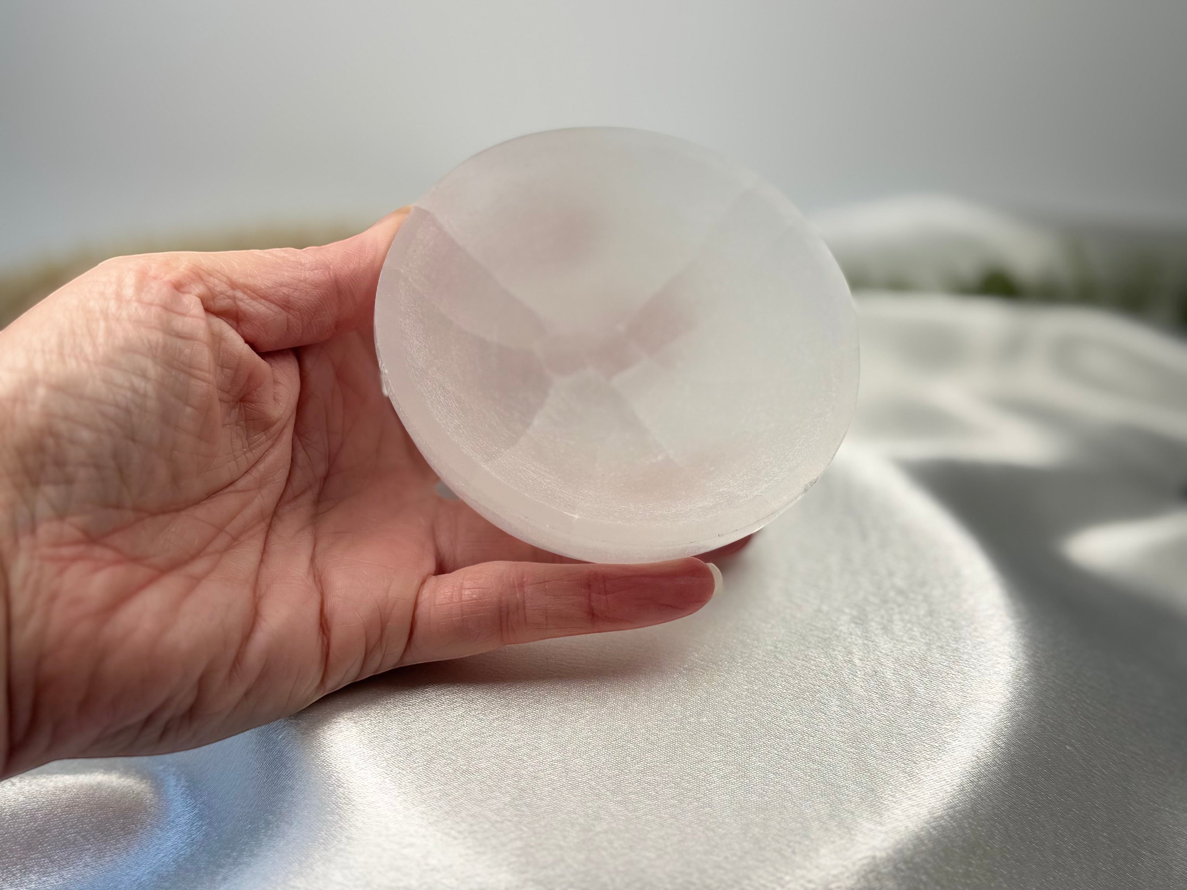 Treasured Energies hand carved white selenite crystal bowl held in a hand against a soft satin background