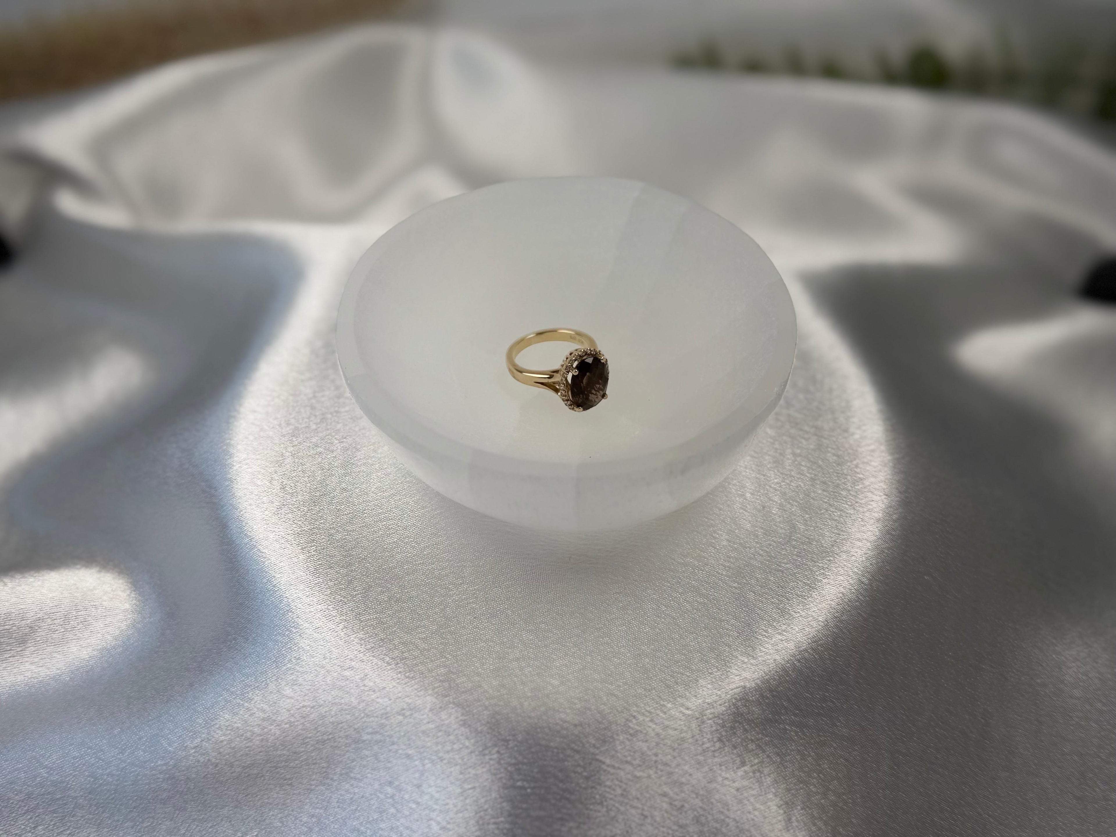 Treasured Energies hand carved white selenite crystal bowl holding a gold gemstone ring on a satin fabric background