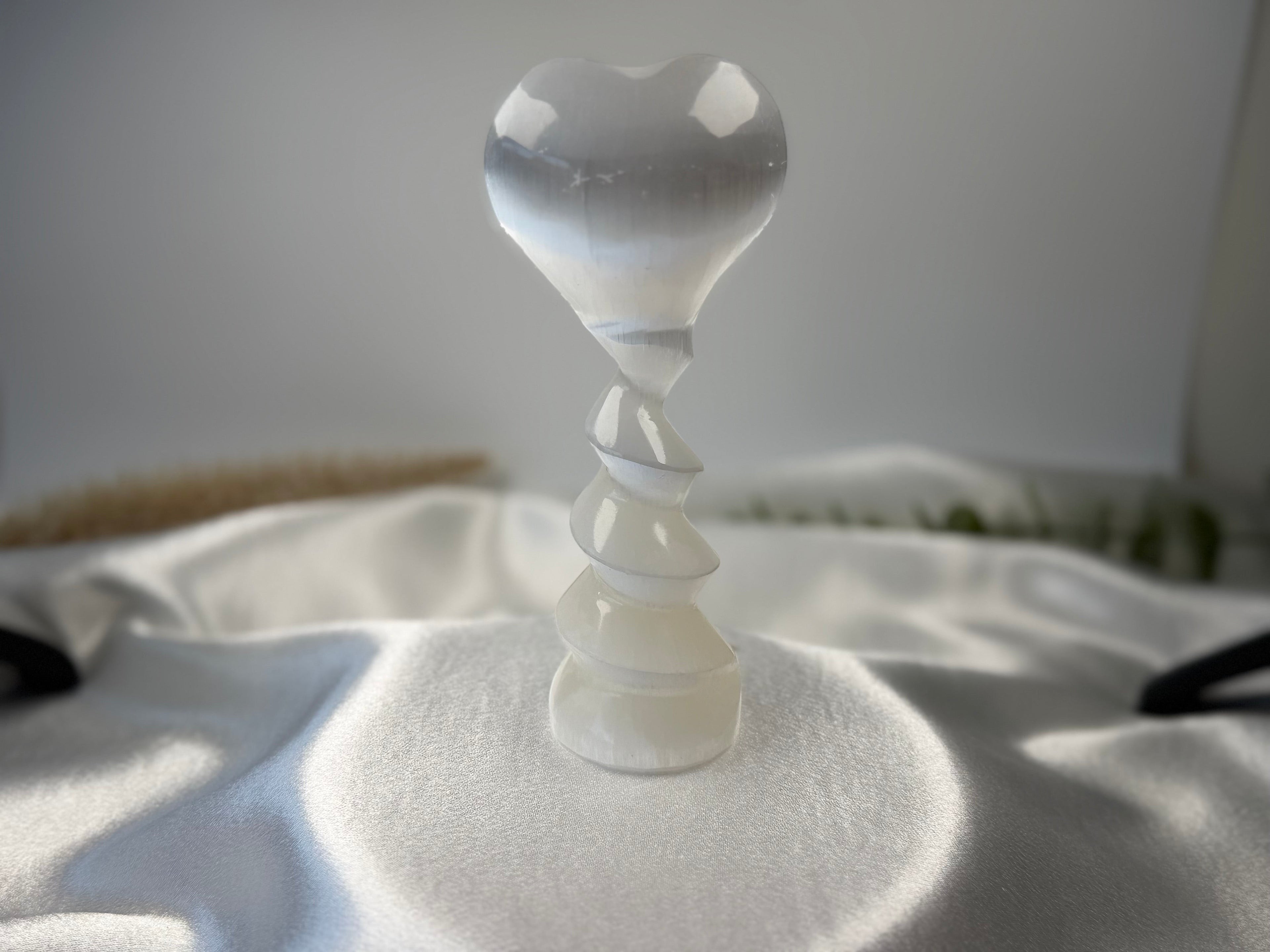 Treasured Energies white selenite crystal heart sculpture with a spiral pedestal base on a satin fabric surface