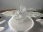 Treasured Energies hand-carved white selenite crescent moon crystal sculpture resting on a white satin fabric surface.