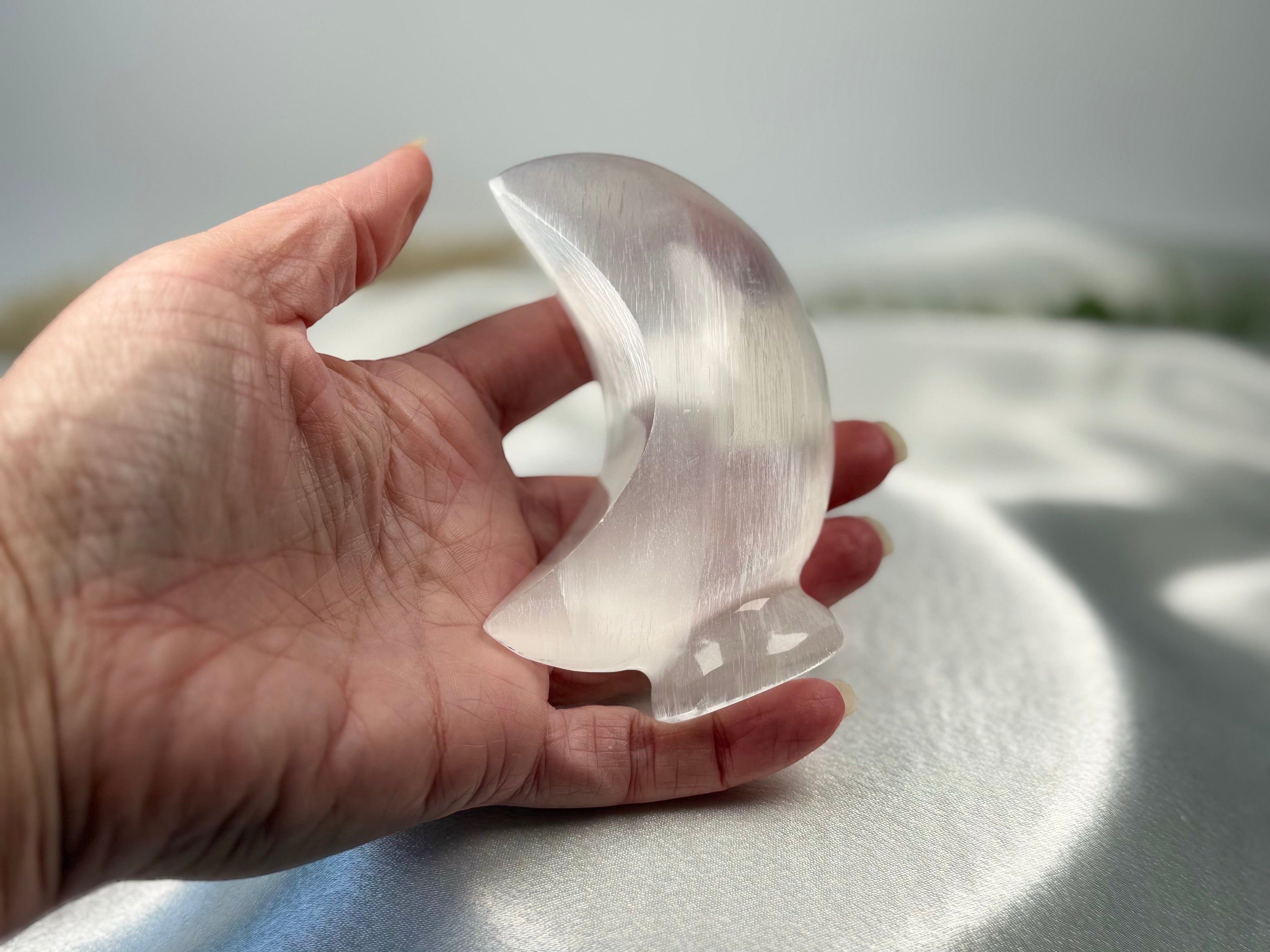Treasured Energies hand-carved translucent white selenite crescent moon crystal sculpture held in a palm