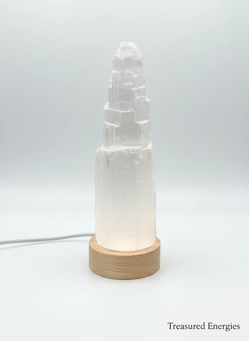 Treasured Energies small selenite crystal tower lamp with a round wooden LED base glowing against a white background.