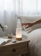 Treasured Energies small selenite tower lamp with LED base glowing on a wooden nightstand in a serene bedroom setting