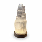 Treasured Energies small selenite tower lamp with a glowing LED light on a dark wooden base against a white background