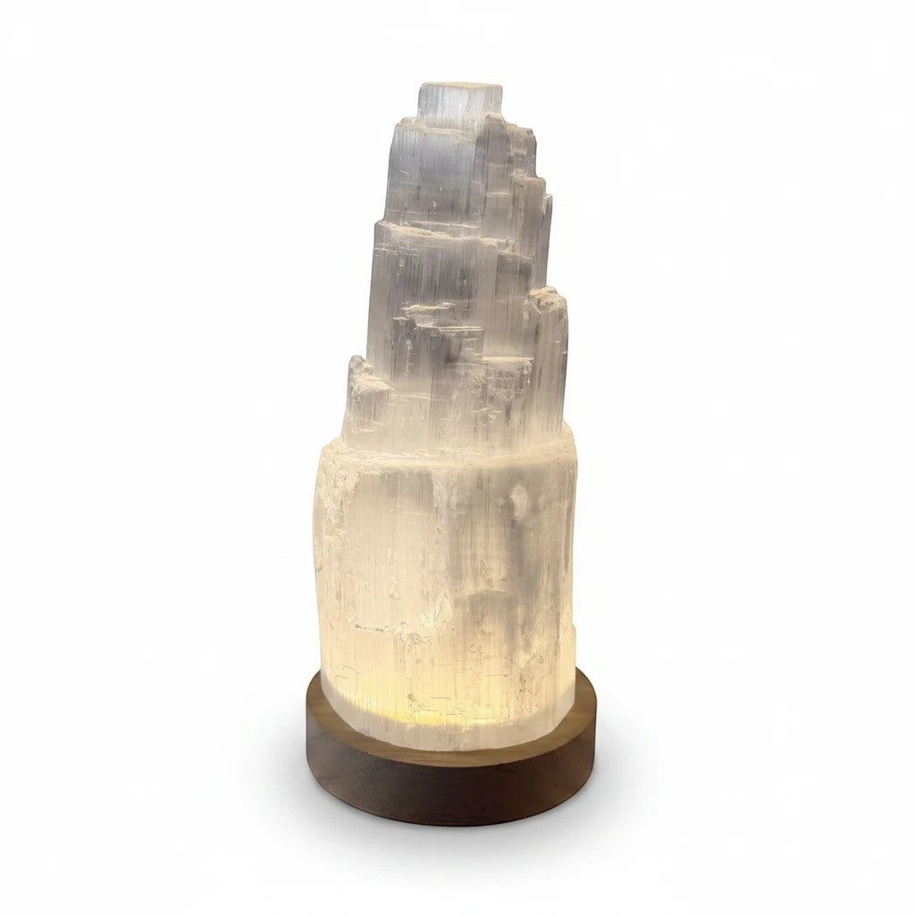 Treasured Energies small selenite tower lamp with a glowing LED light on a dark wooden base against a white background