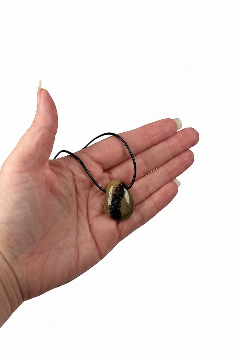 Treasured Energies polished Septarian pendant necklace held in a palm, showing brown and yellow mineral patterns.