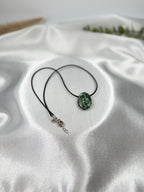 Treasured Energies seraphinite crystal pendant on a simple black cord necklace resting on white satin fabric.