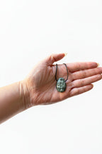 Treasured Energies seraphinite crystal pendant on a black cord held in a palm for healing and chakra alignment