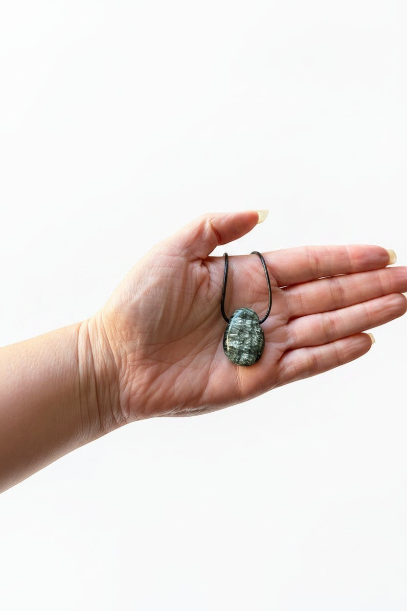 Treasured Energies seraphinite crystal pendant on a black cord held in a palm for healing and chakra alignment