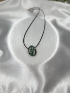 Treasured Energies seraphinite crystal pendant on a black cord necklace against a white satin background