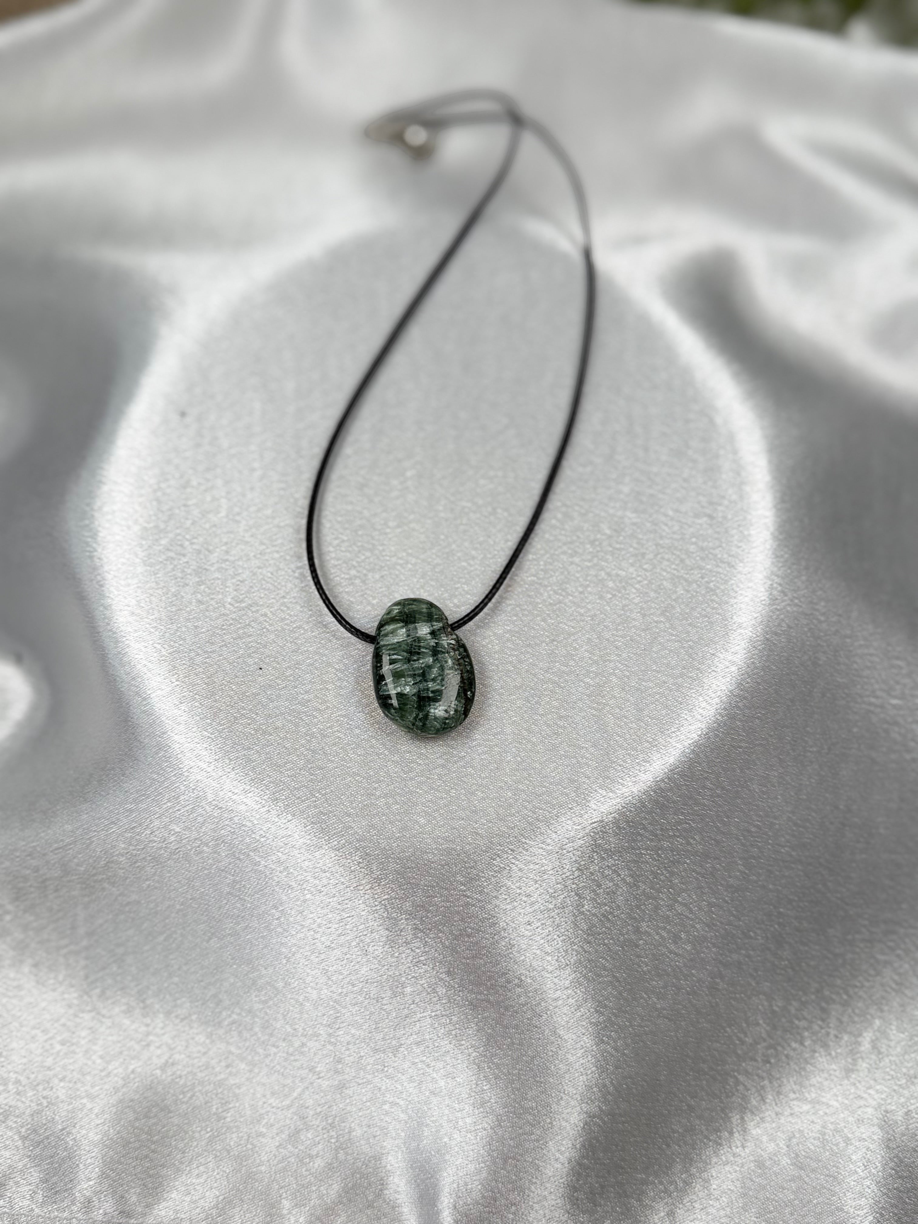 Treasured Energies seraphinite crystal pendant on a black cord necklace against a white satin background