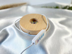 Treasured Energies small round wooden LED lamp base with white control cable on a soft white satin fabric background