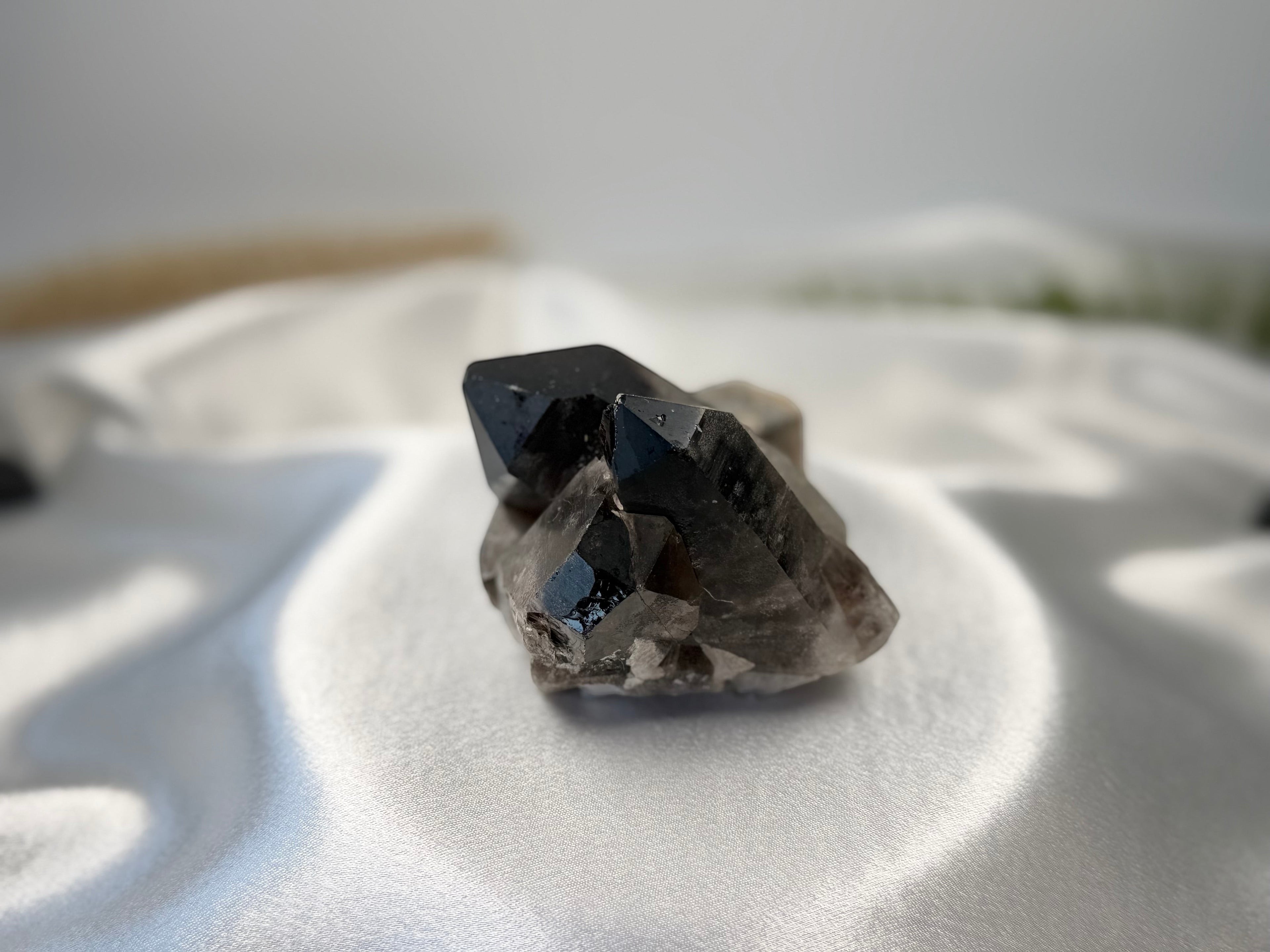 Treasured Energies raw smoky quartz crystal cluster with deep grey and brown points on a white satin background