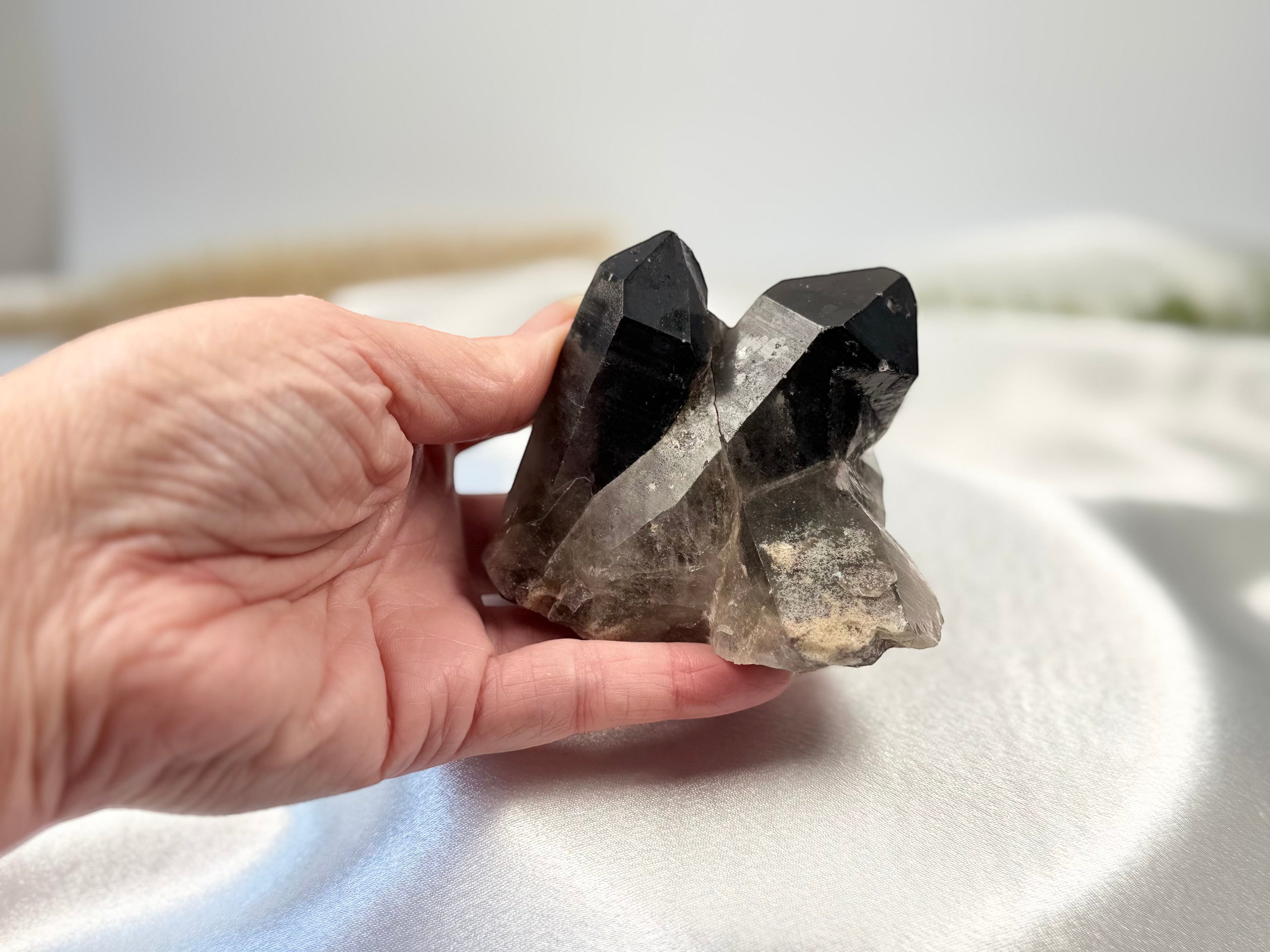 Treasured Energies raw smoky quartz crystal cluster held in hand, featuring deep brown and grey translucent points.