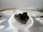 Treasured Energies raw smoky quartz crystal cluster with dark grey pointed terminations on a white satin background.