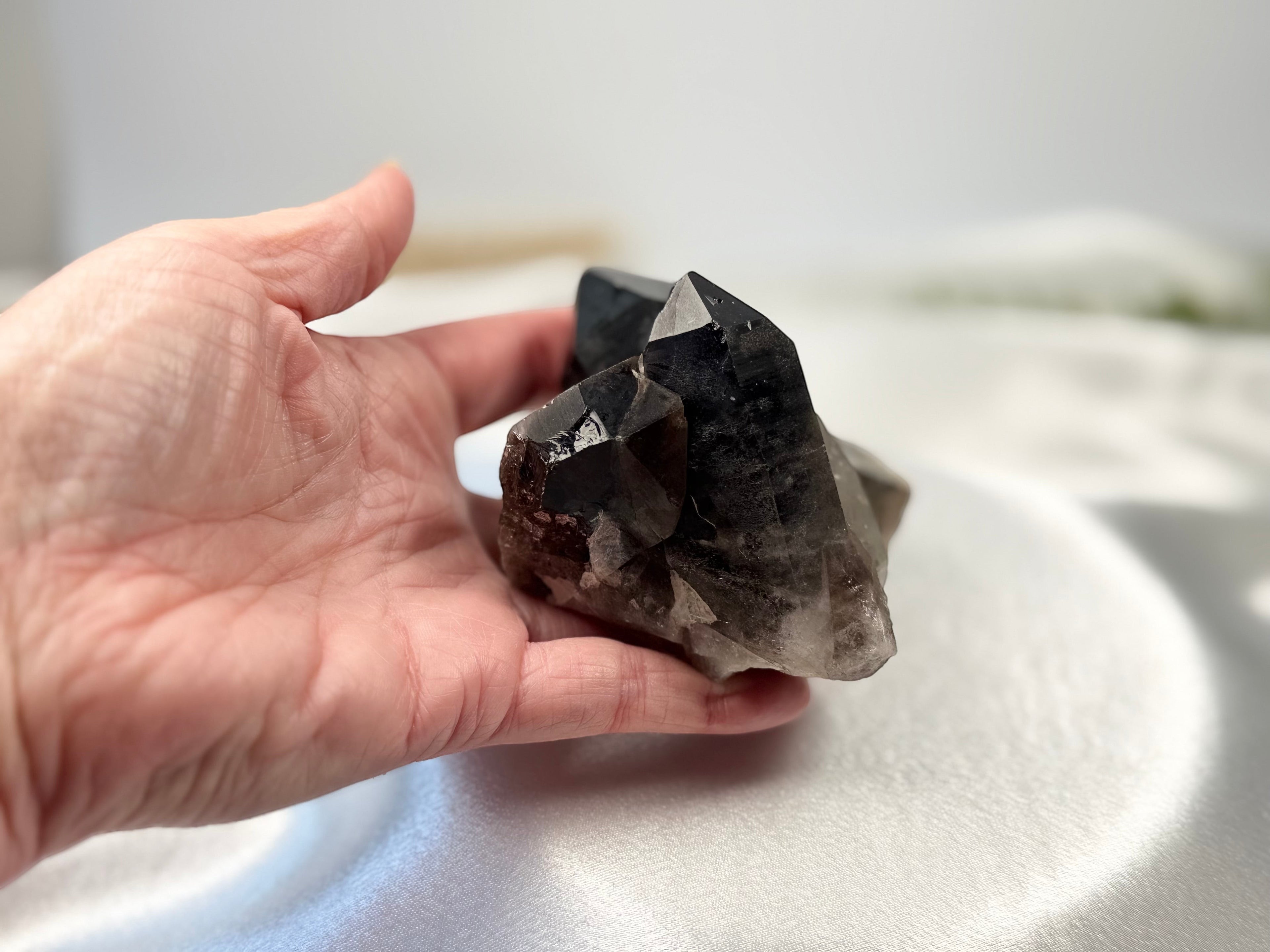Treasured Energies raw smoky quartz crystal cluster held in a hand, showcasing deep brown and grey translucent points.