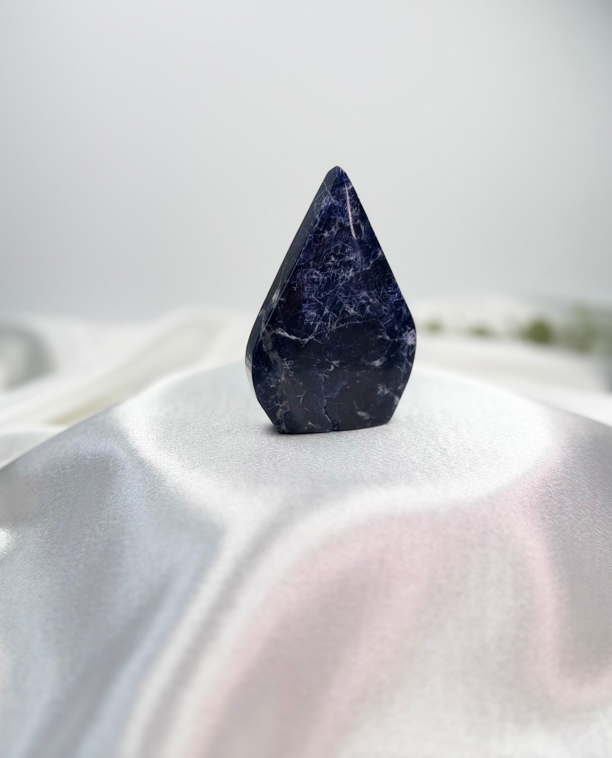 Treasured Energies polished royal blue Sodalite crystal flame sculpture with white mineral veining on a white cloth.