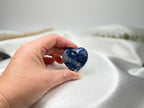 Treasured Energies polished blue and white sodalite crystal heart held in a hand against a white satin background.