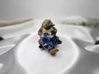 Treasured Energies polished blue sodalite crystal heart held by a small platypus figurine on white satin fabric.