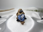 Treasured Energies polished blue sodalite crystal heart held by a small platypus figurine on white satin fabric