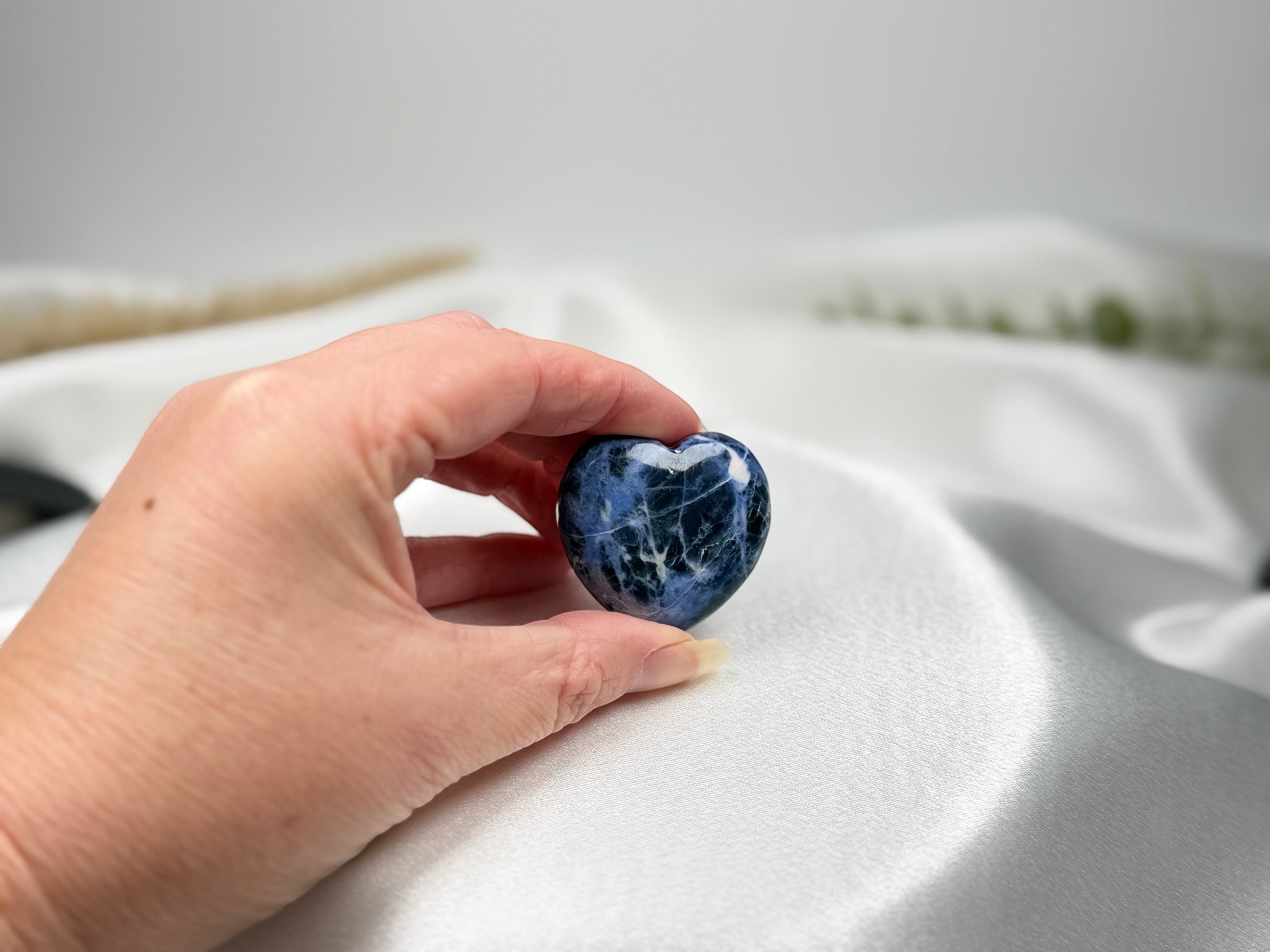 Treasured Energies polished blue sodalite crystal heart held in a hand against a soft white satin background.